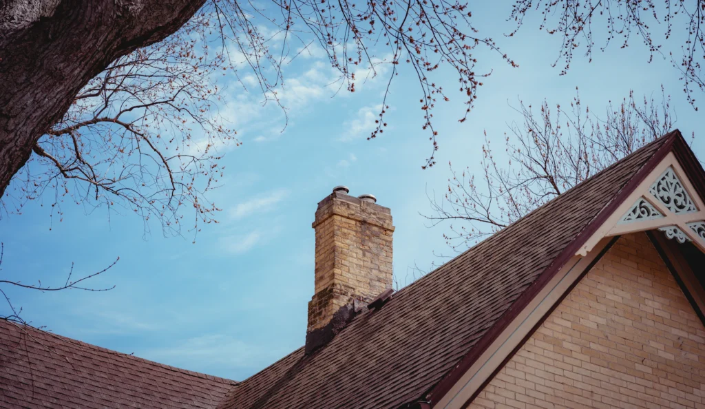 Brick chimney beside a gable roof under a blue sky