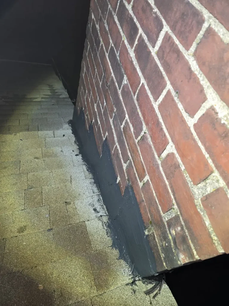 Roof junction and flashing repair area beside the brick chimney in Milltown